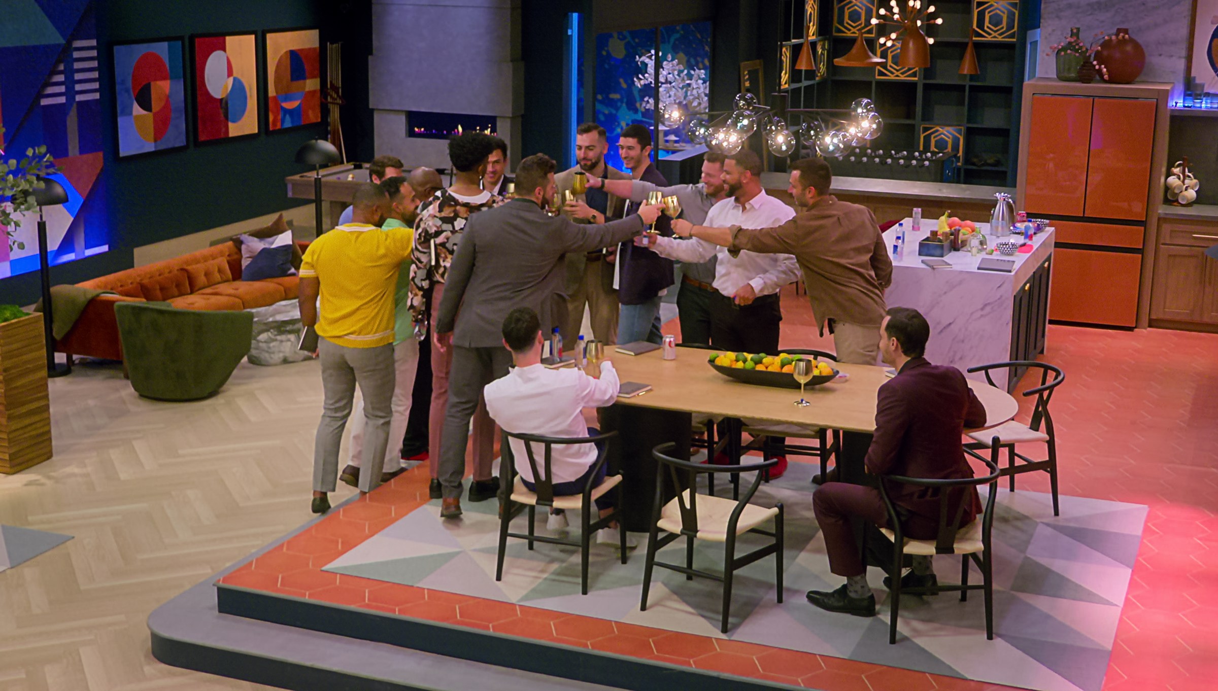 A group of men sit and stand around a long table, all dressed in suits or business casual, raising wine glasses to each other.