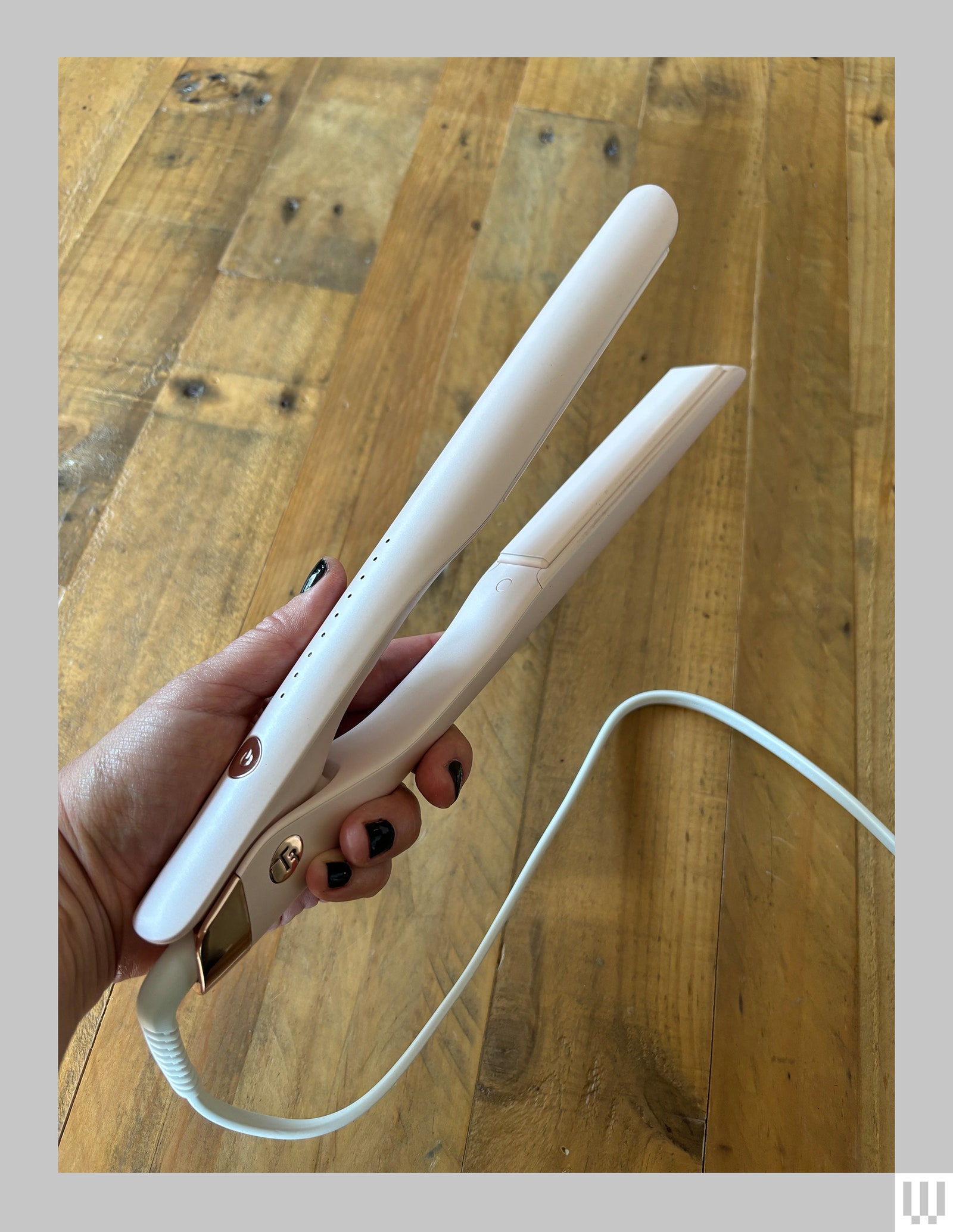 Hand holding a thin white hair straightener showing a pearl colored panel on the inside of one of the clamps