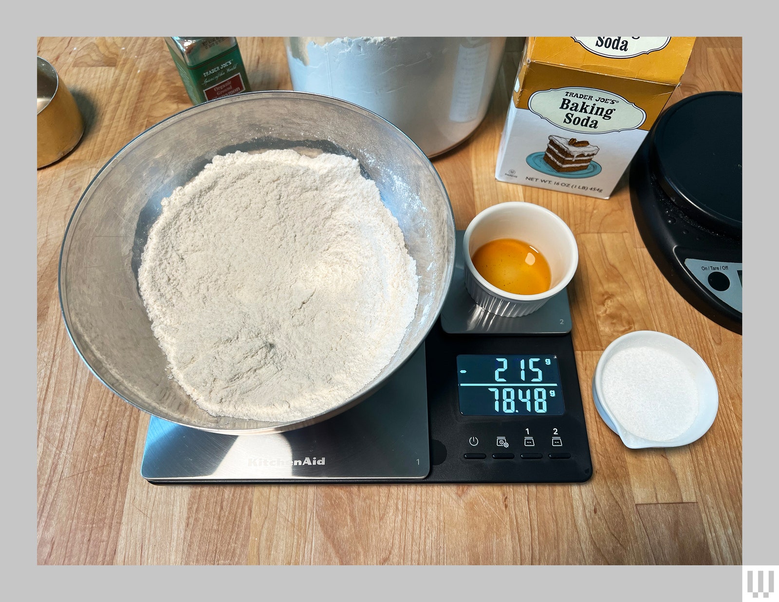 Large black and silver digital scale with a metal bowl of flour and an additional container on top sitting on a kitchen...