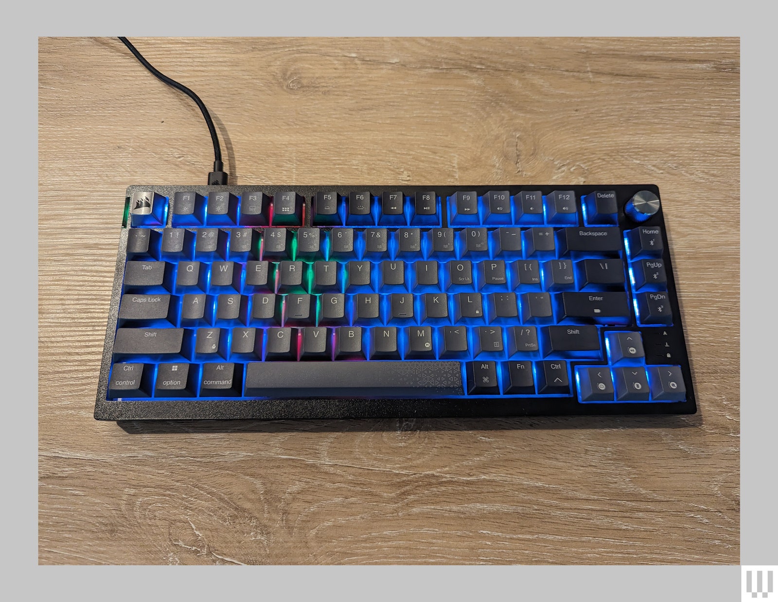 The Corsair k65 keyboard in black with RGB lights on a wood surface.