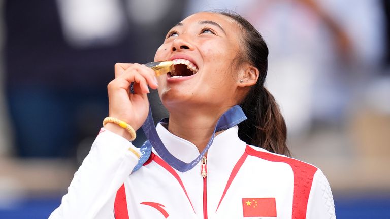 China's Zheng Qinwen bites her gold medal after defeating Croatia's Donna Vekic during the Women's Singles tennis final at the Roland Garros stadium at the 2024 Summer Olympics, Saturday, Aug. 3, 2024, in Paris, France. (AP Photo/Manu Fernandez)