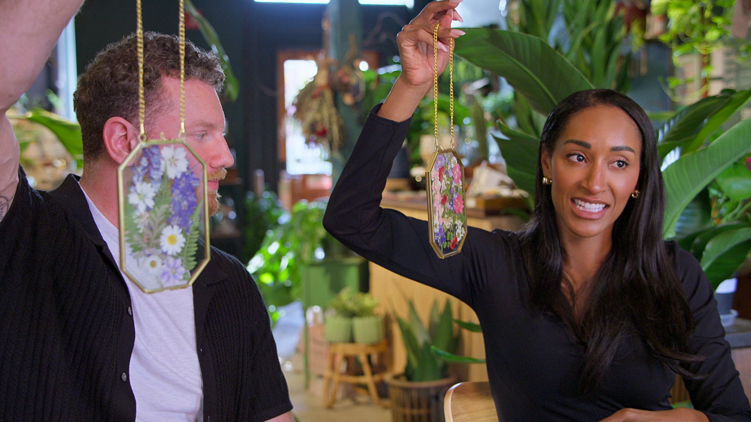 A man and a woman hold up glass ornamentation made from pressed flowers.