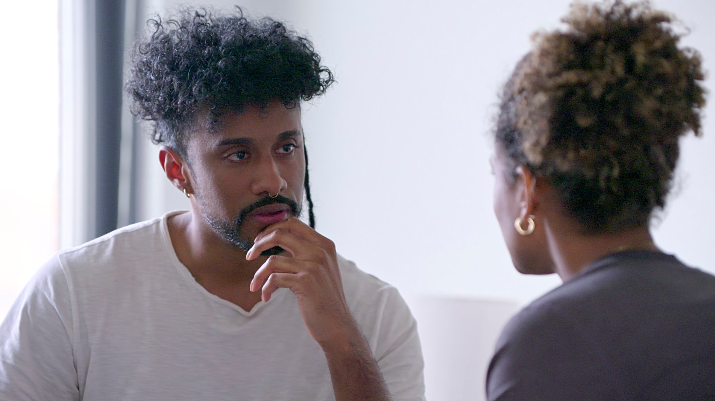 A man sits with his hand to his chin, speaking to a woman we see in profile.