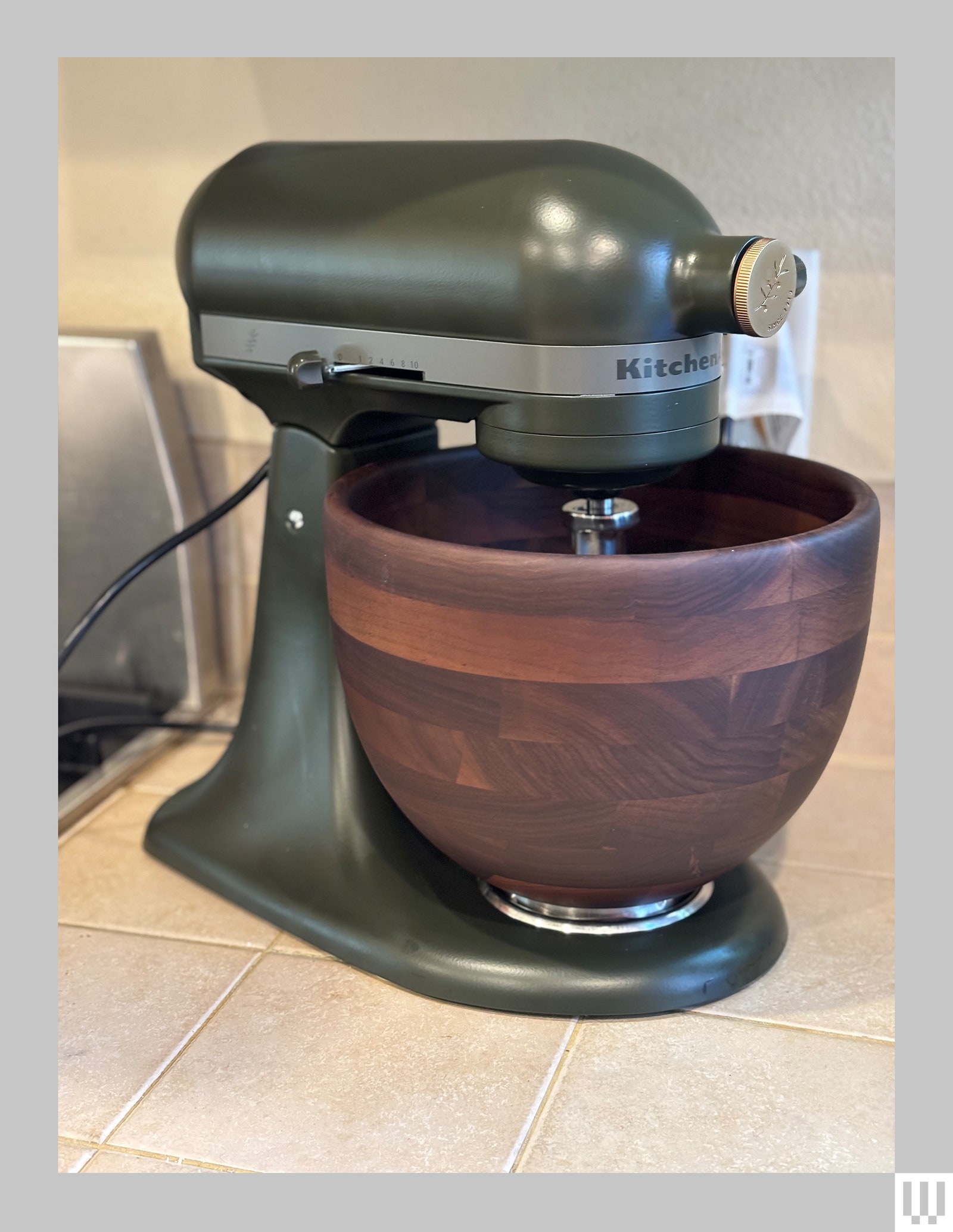 Side view of the KitchenAid Evergreen Stand Mixer a green appliance with large wooden bowl sitting on a kitchen counter