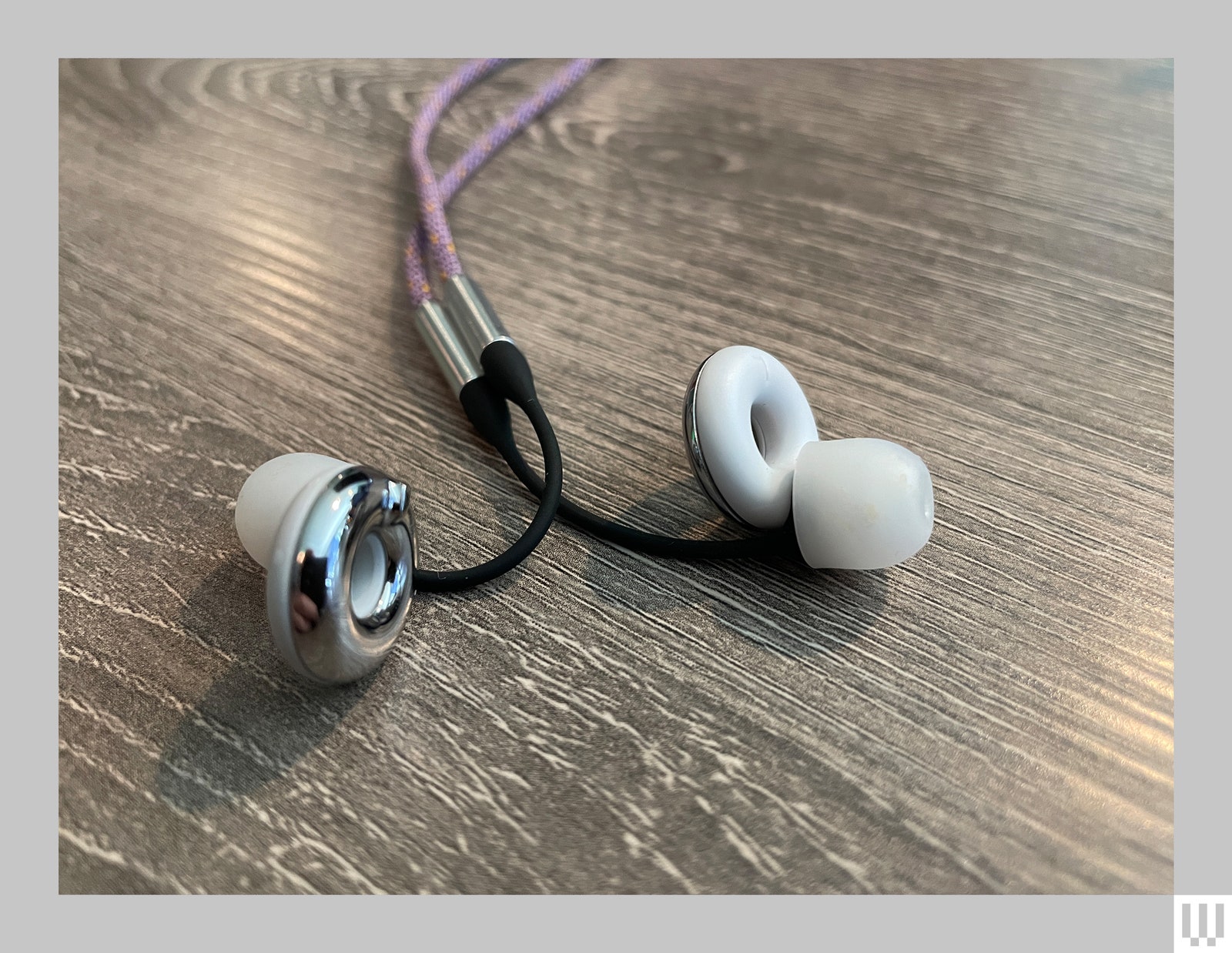 The Loop Switch 2 earplugs sitting on a wooden surface 2 white earbuds with a cushion on one end and a thick circular...