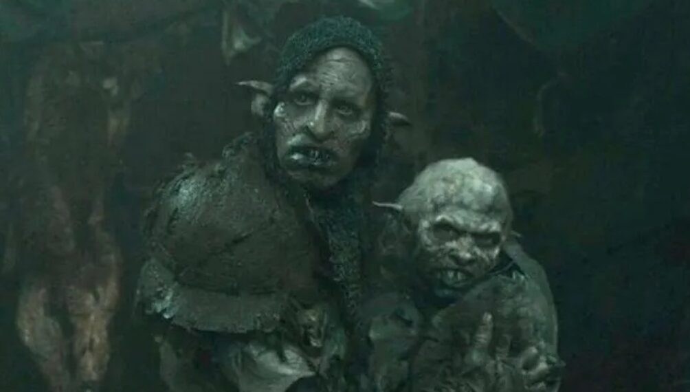 A tall orc with a shorter orc, who is holding a bundle, their orc baby.