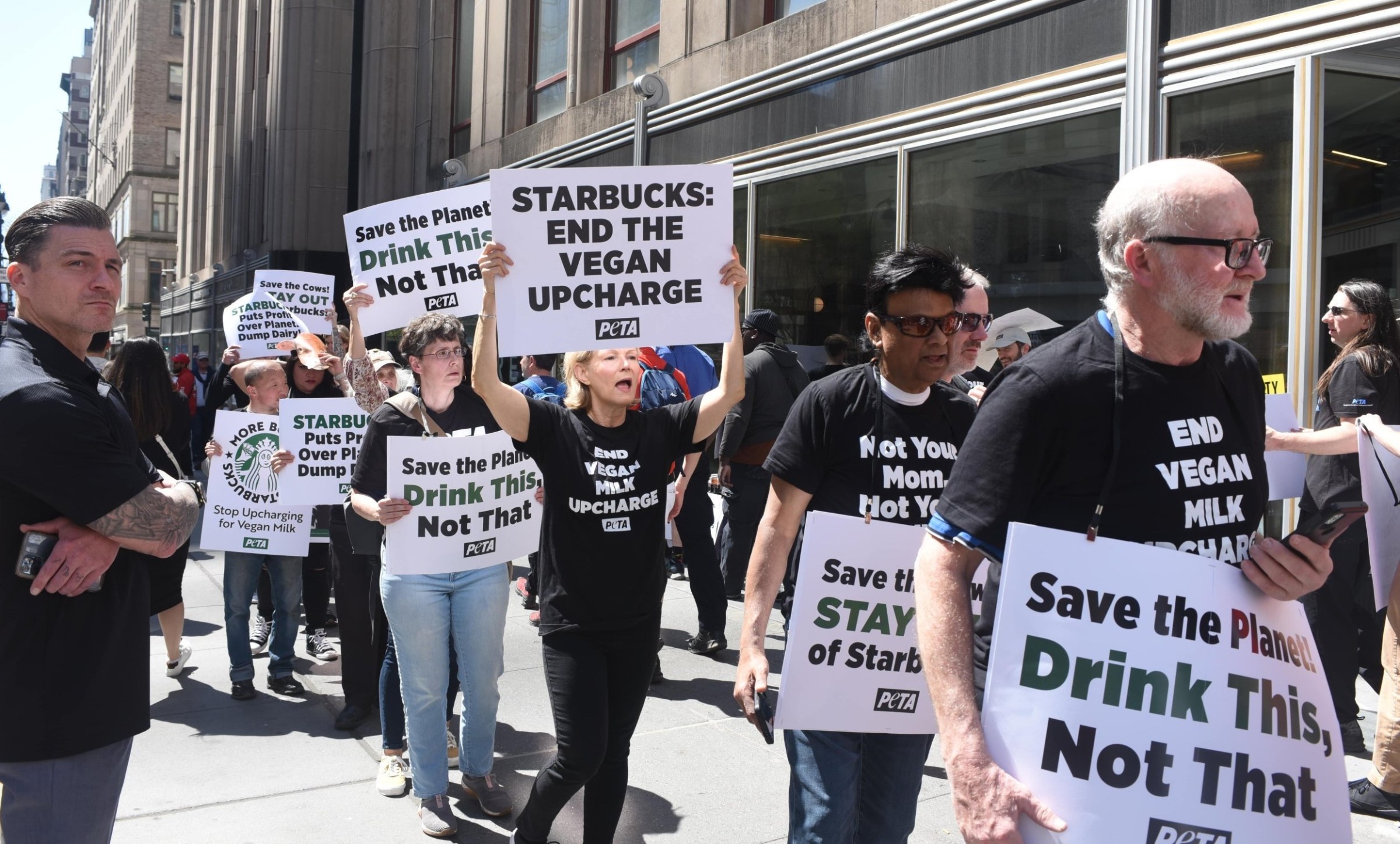 A group of people with protest signs protest Starbucks’s plant-based upcharge. 