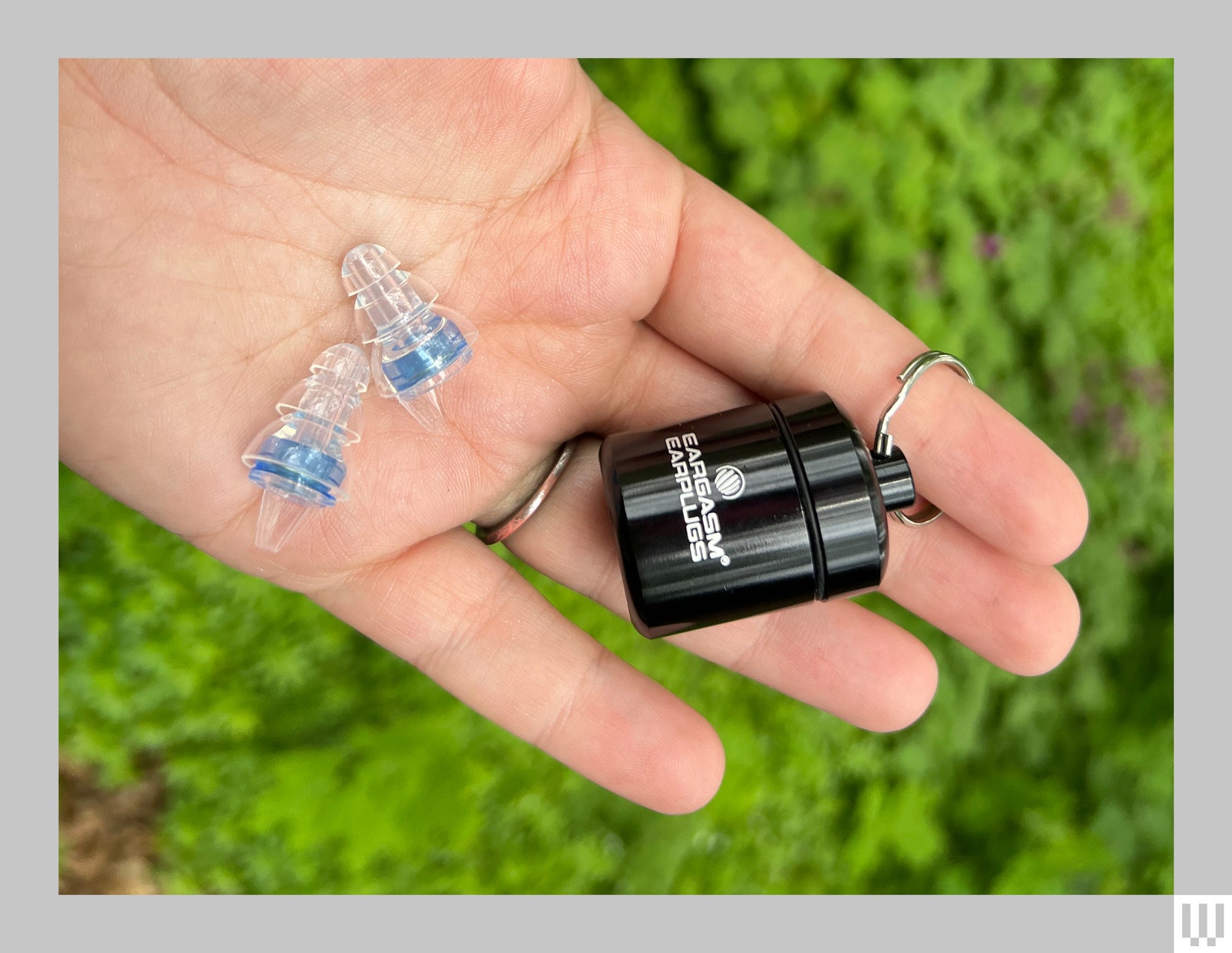 Hand holding small black canister on a keyring and 2 clear ear cushions