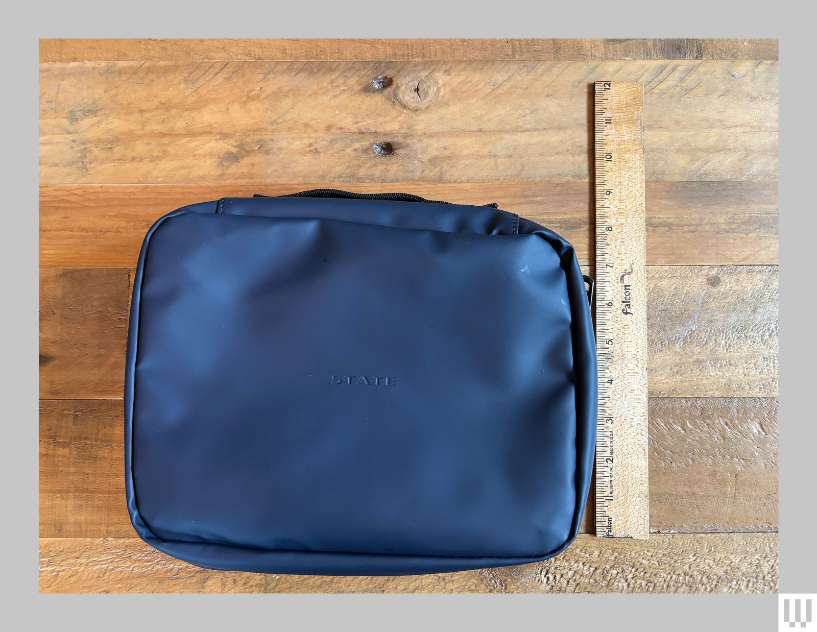 State Bags Benson Toiletry Kit a blue zippered pouch on top a wooden surface