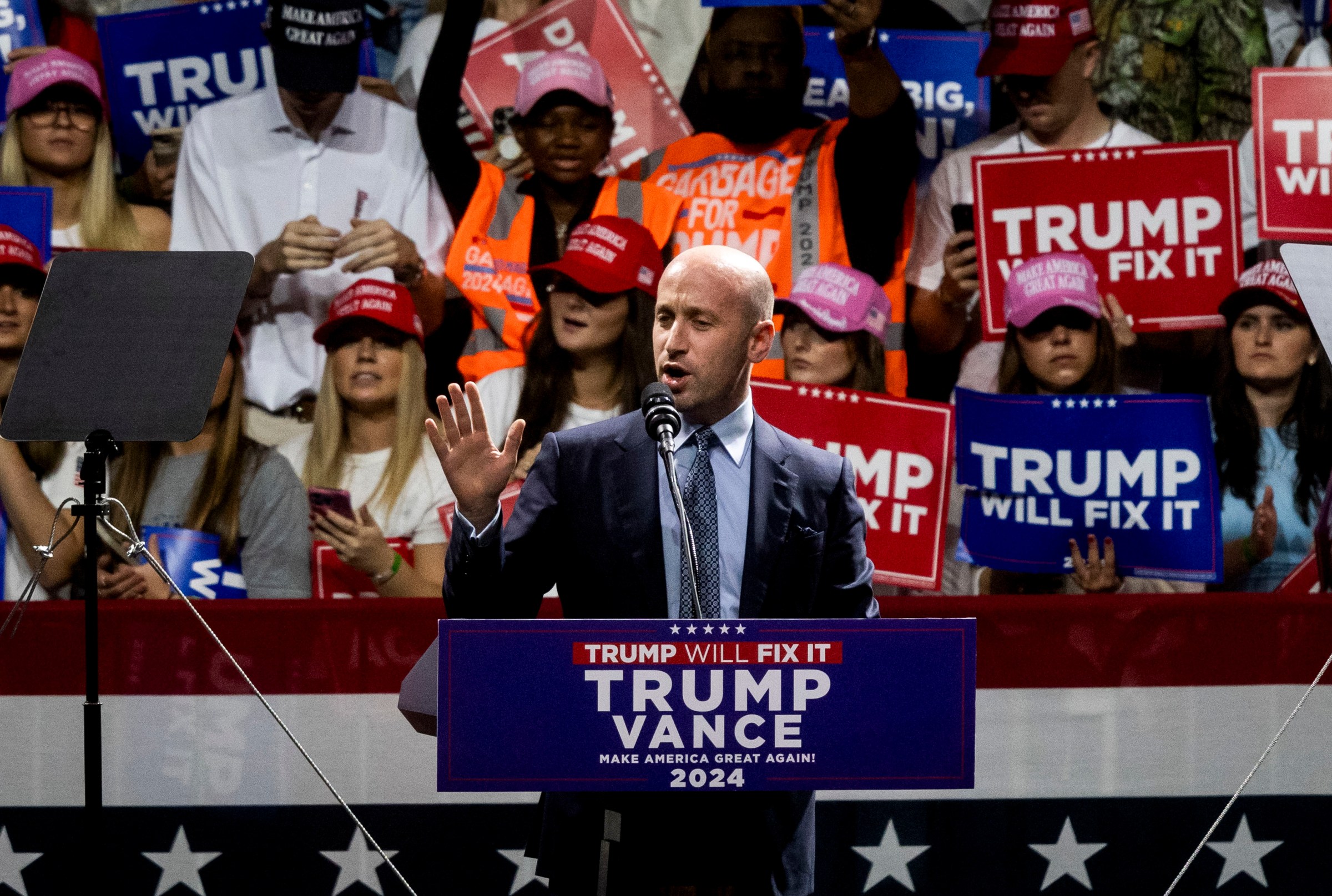 Stephen Miller speaking at a Trump rally. The crowd behind him hold “Trump will fix it” signs.