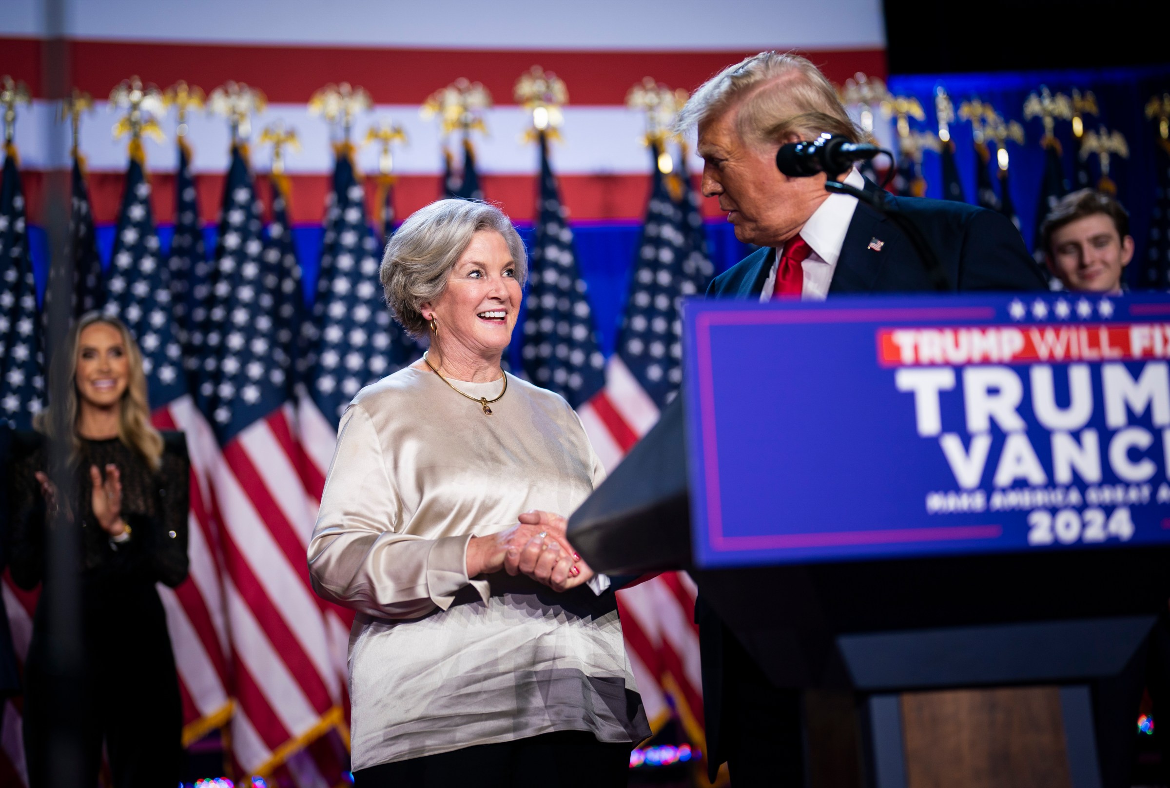 Susie Wiles shaking hands with Trump onstage at a Trump-Vance rally.