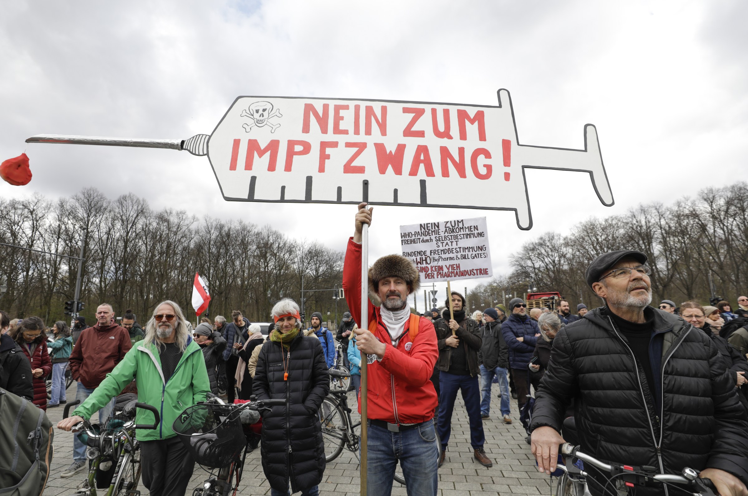 A crowd of demonstrators hold up signs written in German protesting against compulsory vaccination.