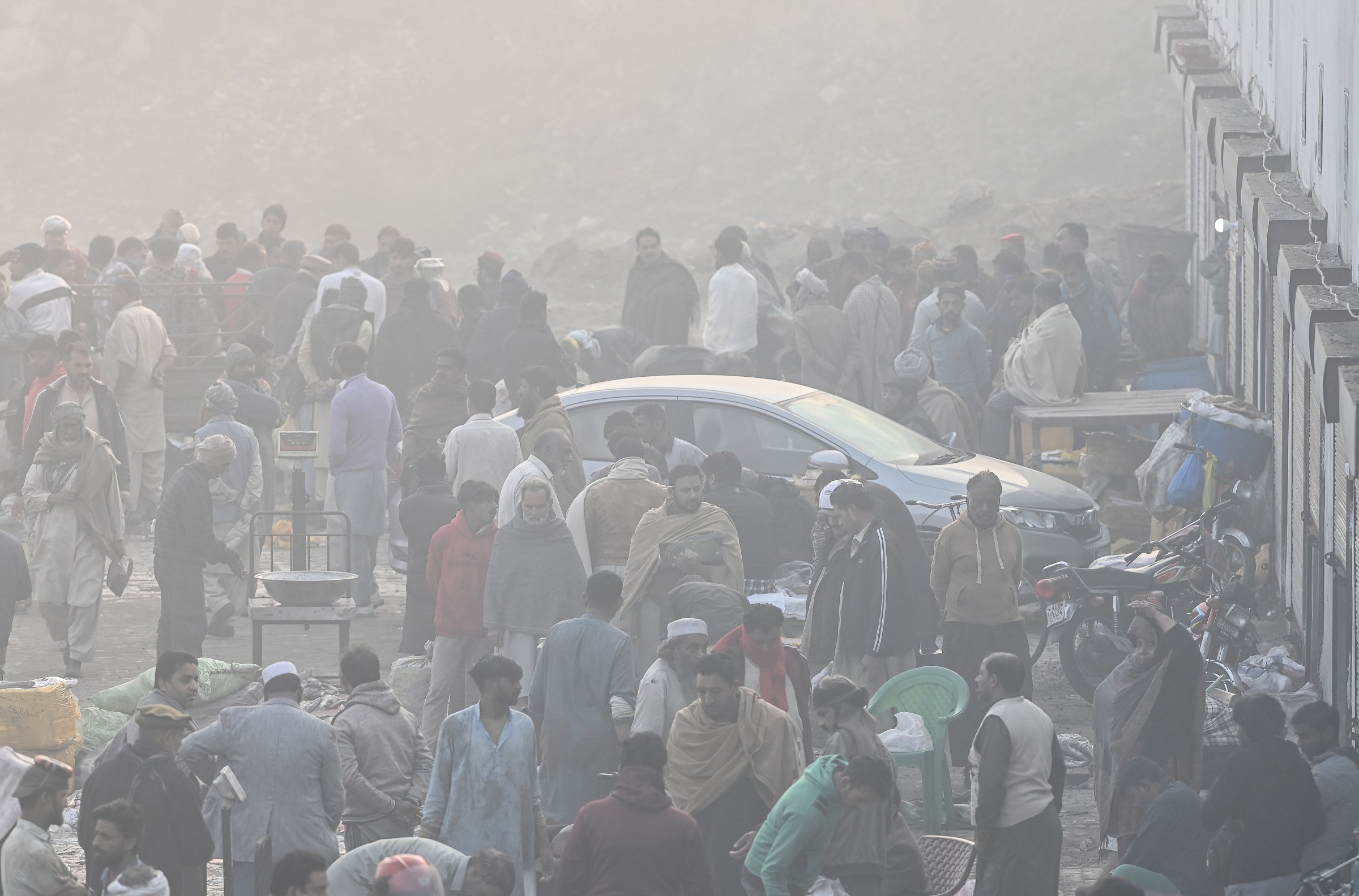 People standing around a parked car on a very smoggy day.