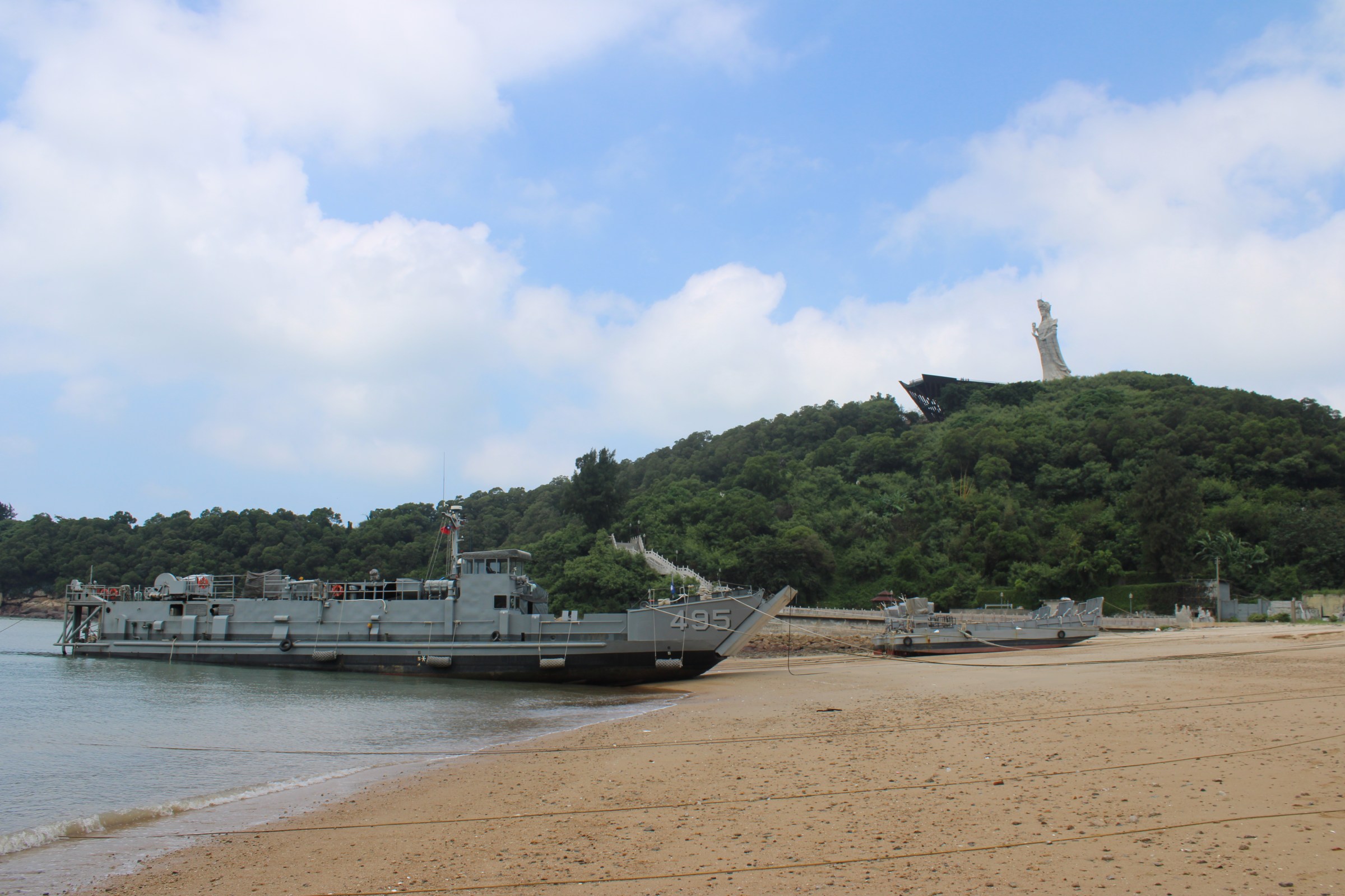 A military ship on a beach below a large female statue.