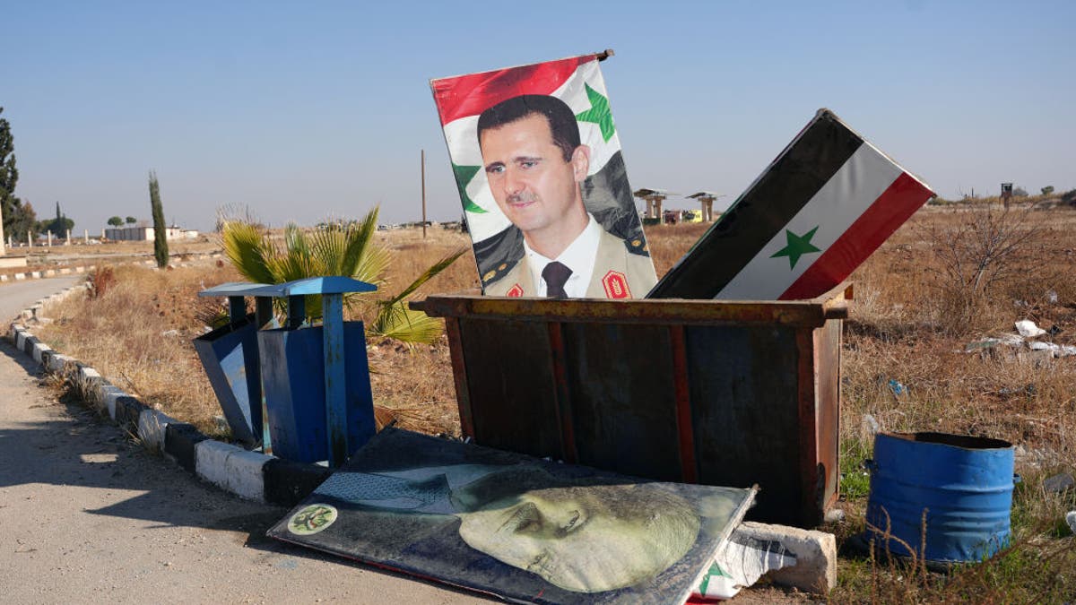 A picture taken at the entrance of the Kweyris military airfield in the eastern part of Aleppo province on Dec. 3, shows a portrait of Syria's President Bashar al-Assad and a national flag in the garbage dumpster following the take over of the area by rebel groups