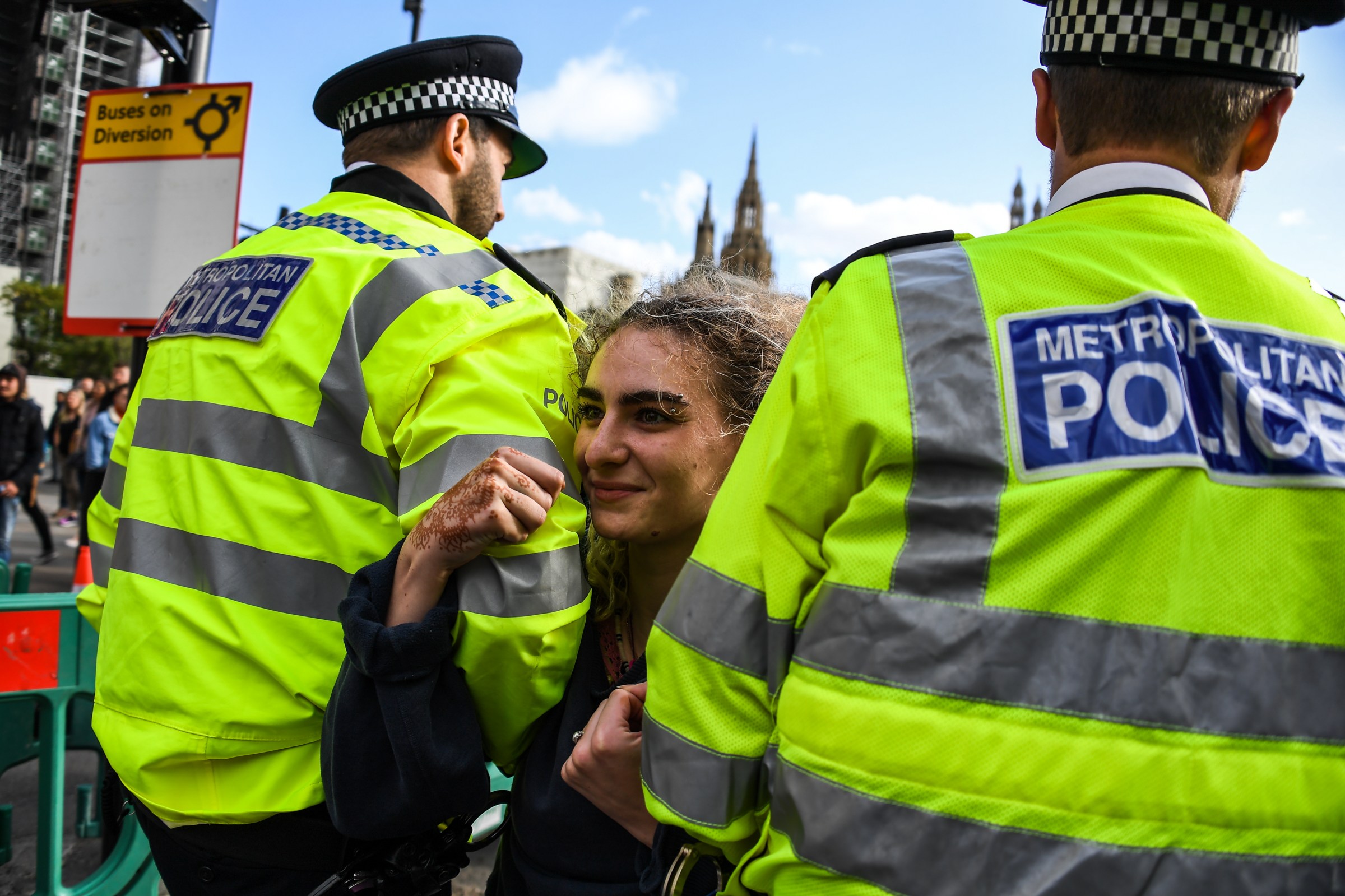 London police officers arrest a smiling Extinction Rebellion activist.
