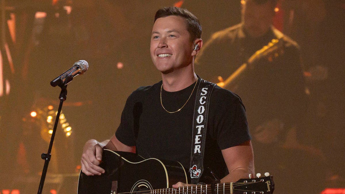 scotty mccreery smiling and holding guitar on stage 