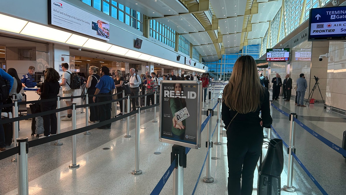 REAL ID sign in a wideshot of an airport full of people.