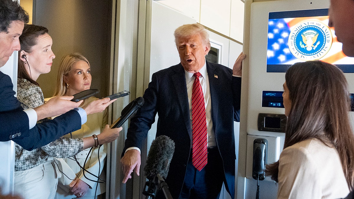 President Donald Trump wearing a red tie stands while he speaks to reporters aboard Air Force One