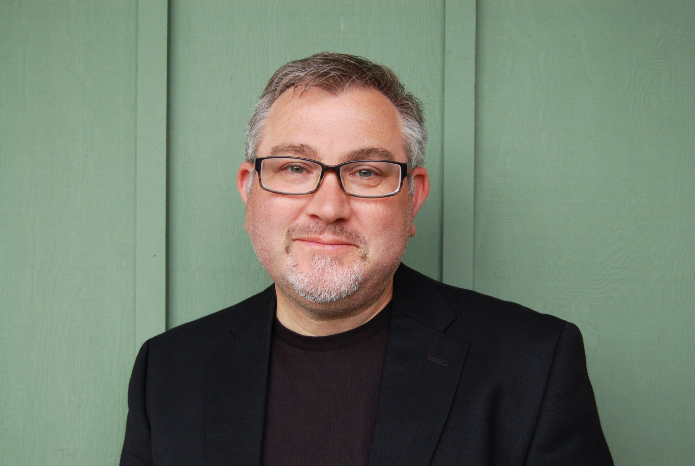 White man with gray hair and facial hear wearing glasses.