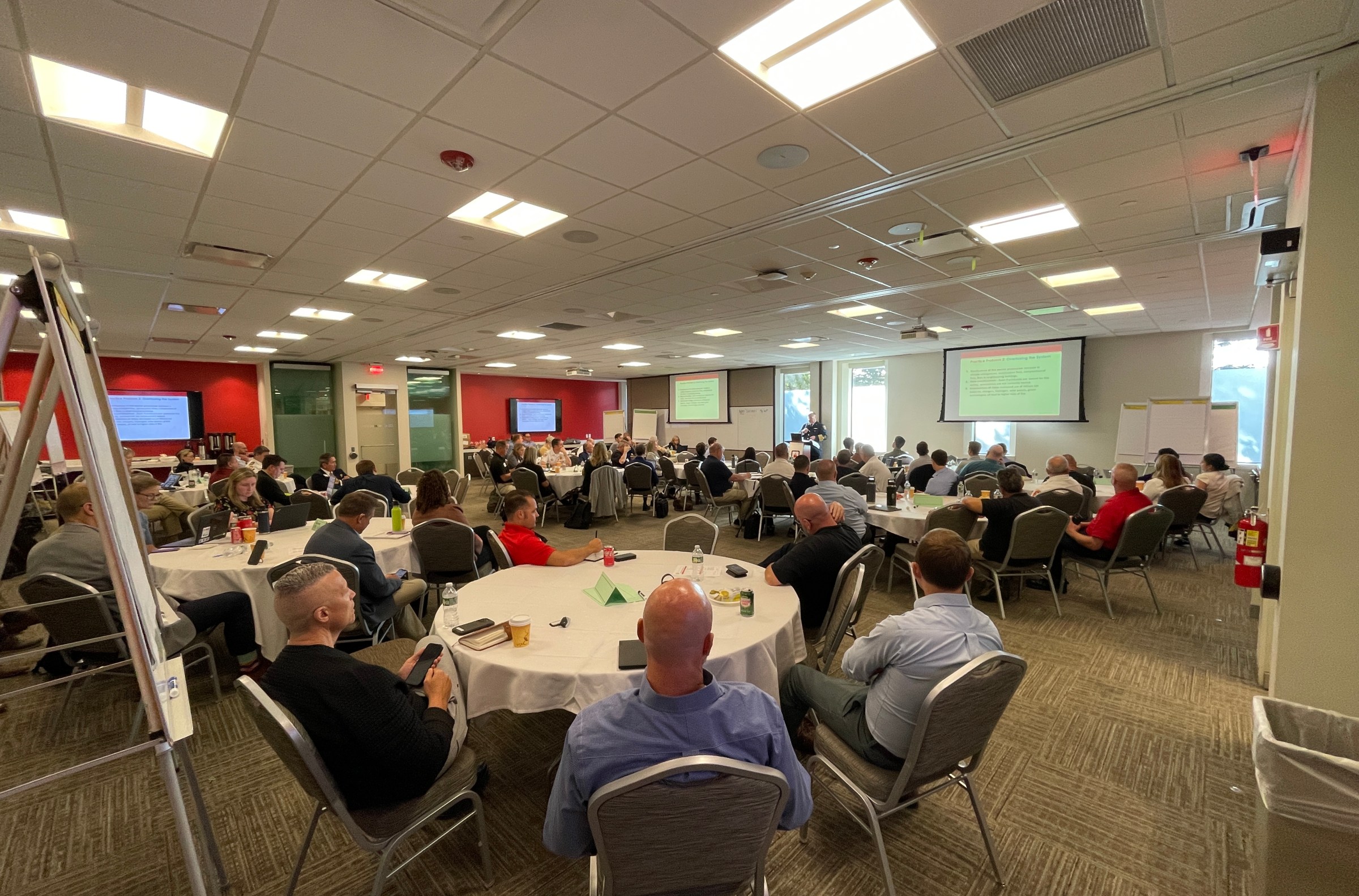 Groups of people, mostly men, sitting around tables in a room.