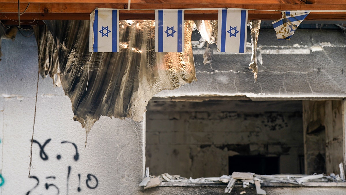 Burned building in Nir Oz with tattered Israeli flags hanging above a blown-out window.