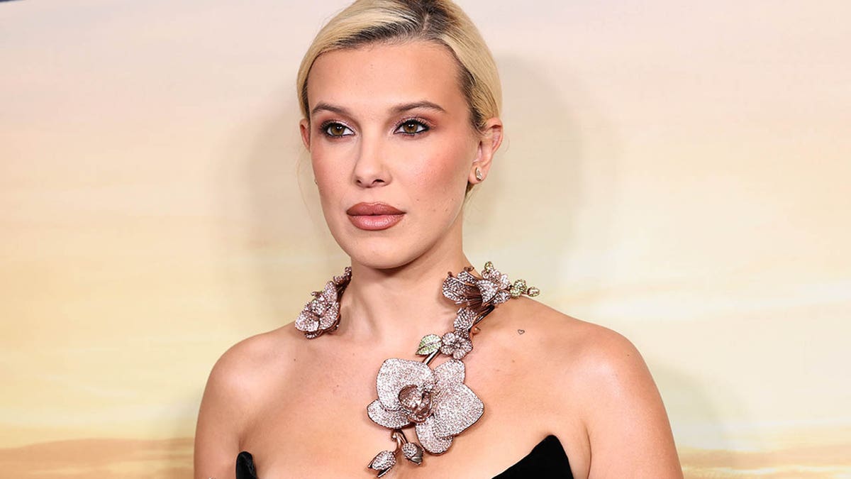 Millie Bobby Brown in black strapless dress on red carpet. 