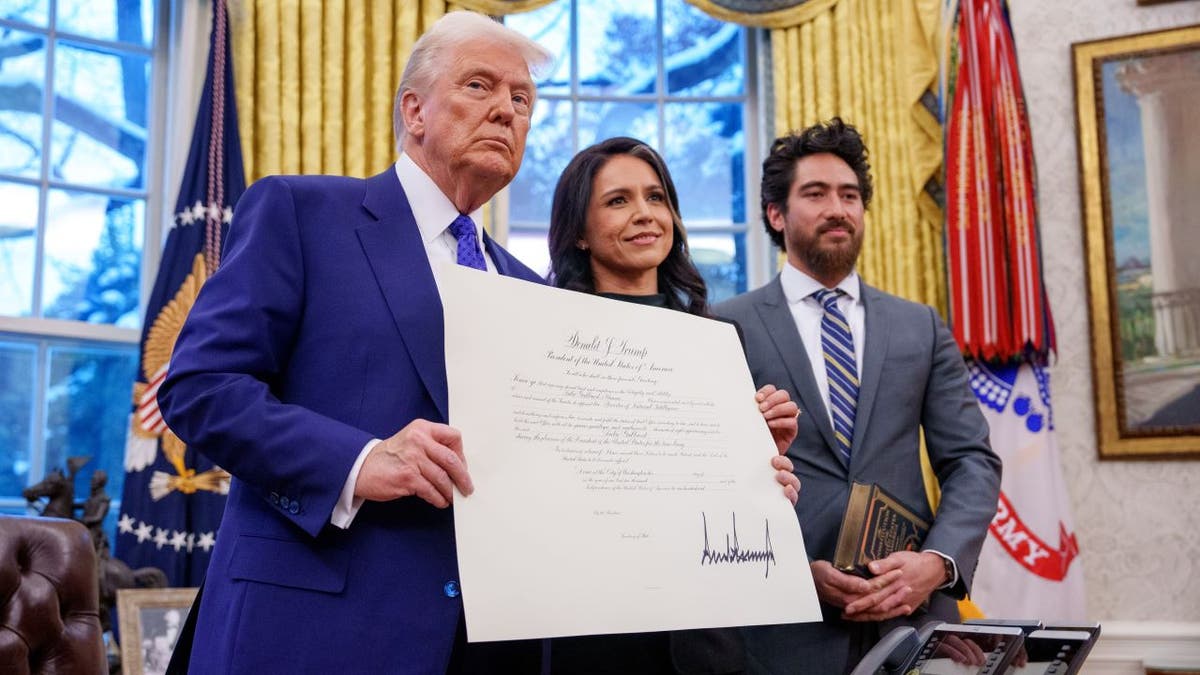 WASHINGTON, DC - FEBRUARY 12: U.S. President Donald Trump, accompanied by Tulsi Gabbard and her husband Abraham Williams, holds up Gabbard's commission for her new role as Director of National Intelligence after she was sworn in, in the Oval Office at the White House on February 12, 2025 in Washington, DC. Gabbard, who will oversee the 18 intelligence agencies and serve as Trump's advisory on intelligence, was confirmed by the Senate 52-48. (Photo by Andrew Harnik/Getty Images)