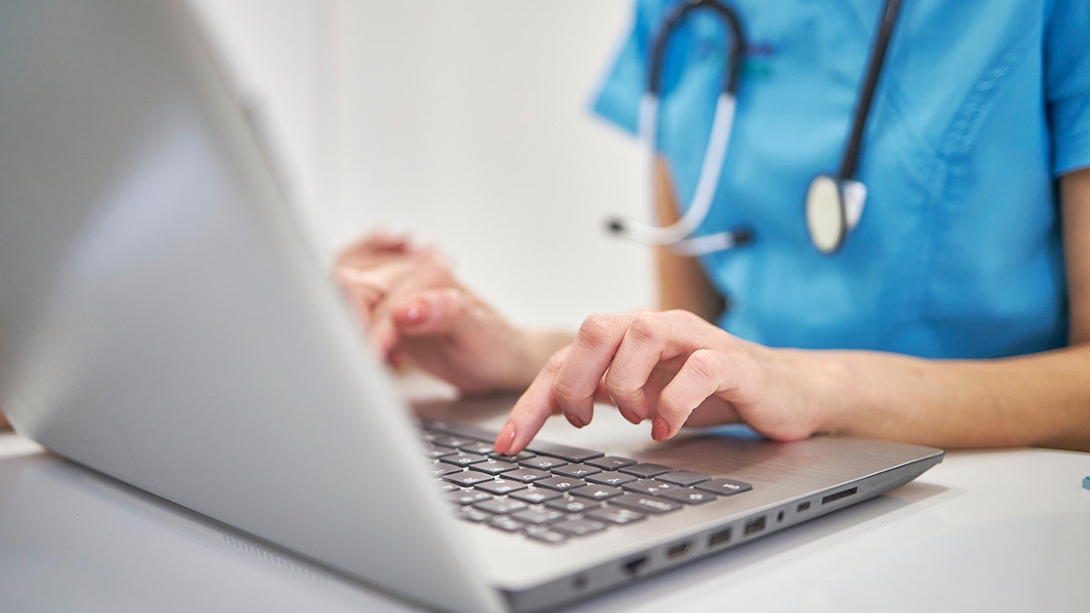 Close-up hands of unrecognizable female physician in medical uniform working typing on laptop keyboard sitting at desk