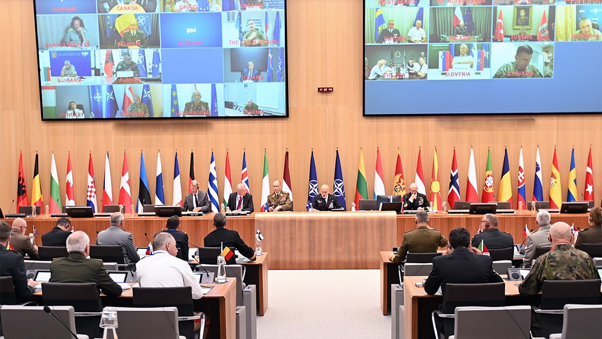 NATO defense chiefs meet in Brussels with large monitors displaying virtual participants from allied nations