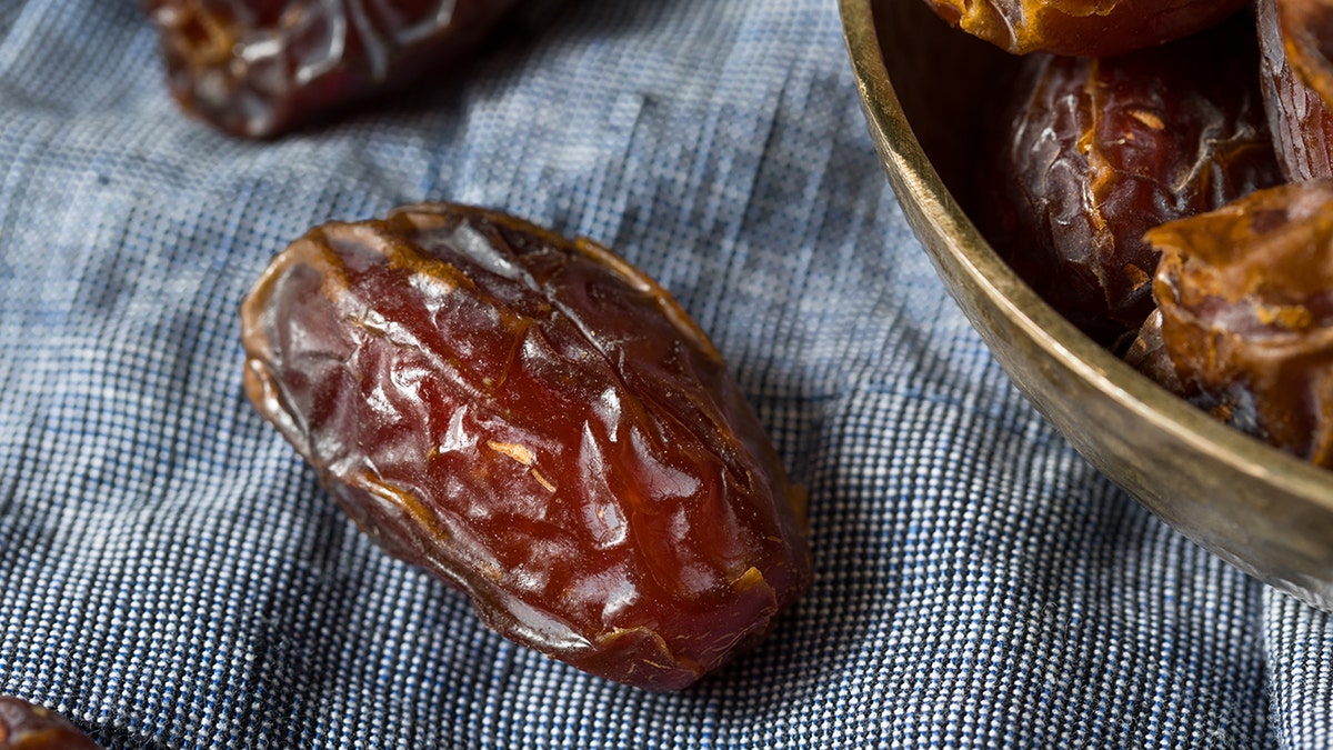 Organic red medjool date seen on tablecloth next to bowl of dates