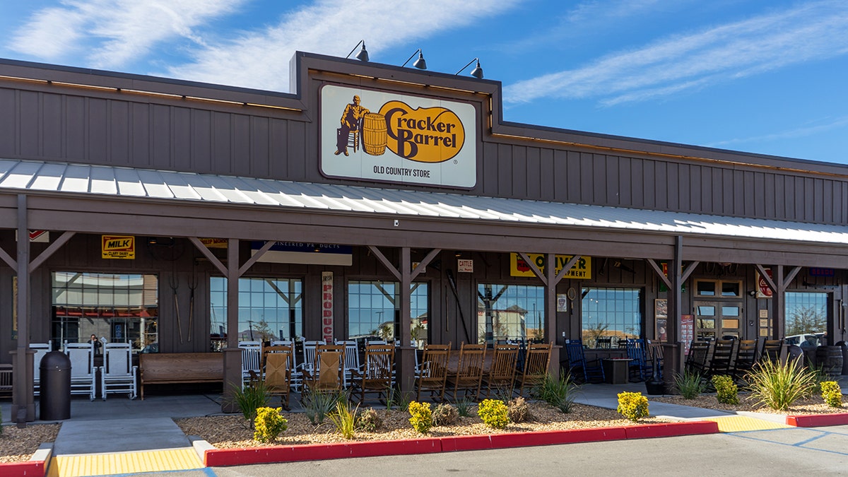 The exterior of a Cracker Barrel Old Country Store with rocking chairs outside is shown.