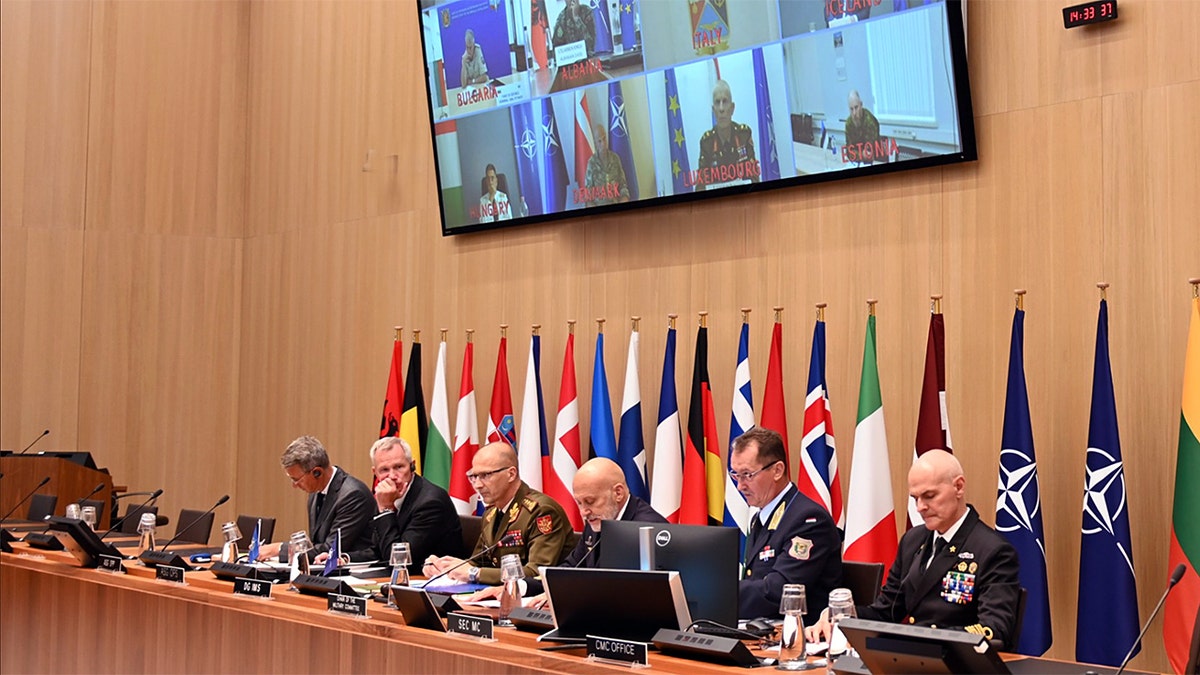 NATO Chiefs of Defense sit at a conference table with flags behind them during a virtual meeting on Ukraine