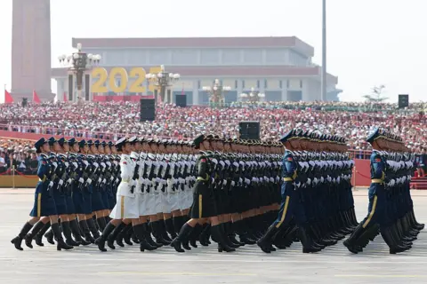 Getty Images Soldiers in ceremonial uniform march in front of a crowded podium