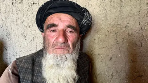 Aakriti Thapar / BBC Ahmad Khan looks at the camera with a grieving expression, as he's pictured in a head-and-shoulders portrait against a light coloured wall.