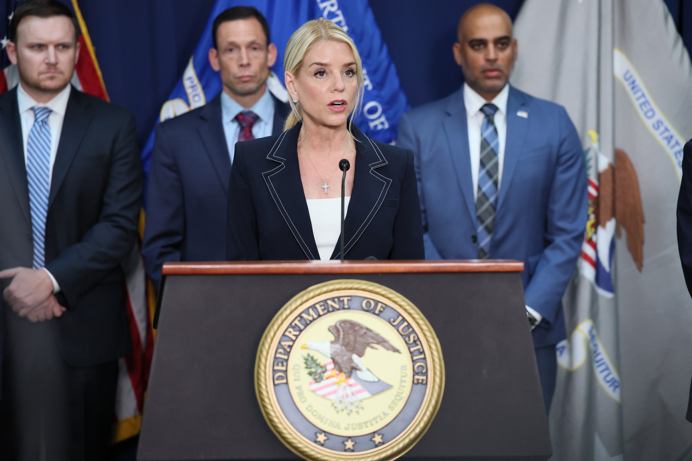 US Attorney General Pam Bondi speaking in front of a DOJ podium.