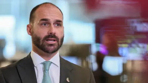 Reuters A bearded man wearing a dark grey suit, aqua patterned tie and a white shirt speaks to camera. He wears a gold pin with the Brazilian and US flags interlocking.