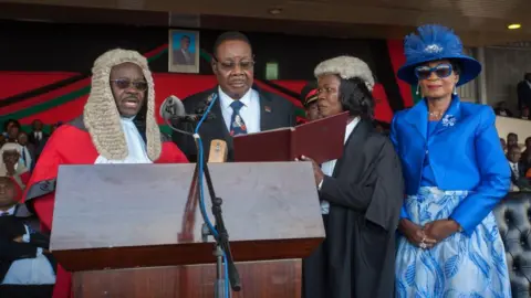 AFP via Getty Images Malawi's President elect Arthur Peter Mutharika is sworn in for his second term by Chief Justice Andrew Nyirenda (L) and Registrar of the high Court and Supreme Court Of appeal (2R) as First Lady Gertrude Mutharika looks onat Kamuzu Stadium in Blantyre on May 28, 2019, after a contentious election marred by allegations of fraud and vote-rigging. - The Malawi Electoral Commission announced on Monday that Mutharika, who heads the ruling Democratic Progressive Party (DPP), had narrowly won last week's vote after an injunction barring the release of the results was lifted. 