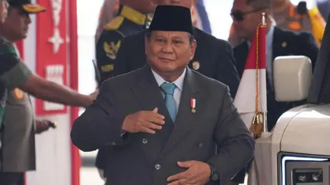 Getty Images Indonesian President Prabowo Subianto passes through a security cordon wearing a suit and with his hands on his jacket.