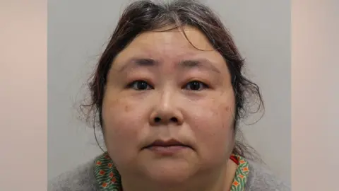 Metropolitan Police A mugshot of Zhimin Qian, pictured staring into the camera. She has curly hair and is dressed in a grey jumper.