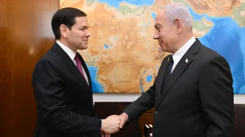 Israel Prime Minister's Office US Secretary of State Marco Rubio (L) and Israeli Prime Minister Benjamin Netanyahu (R) shake hands. They are both wearing suits. 