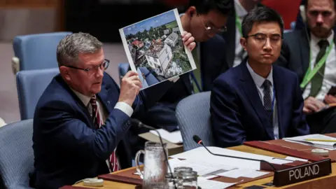 Reuters Poland's Secretary of State Marcin Bosacki holds a photo showing a house with a very damaged roof.