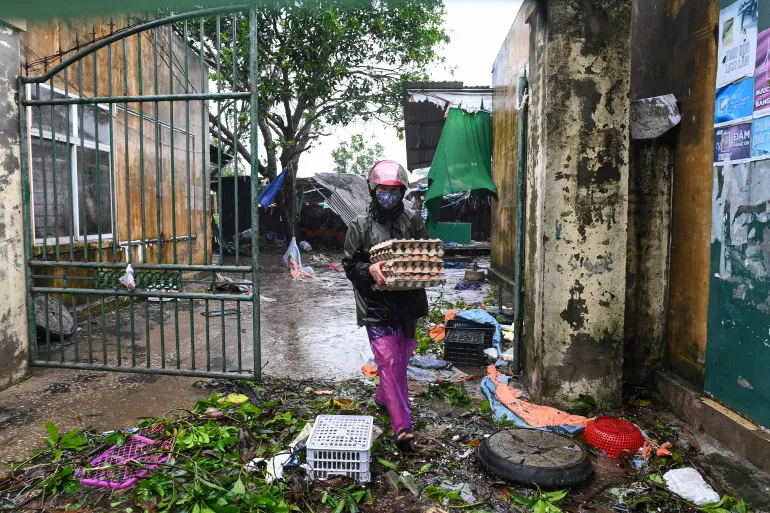 A woman carries belongings as she walks amidst the debris after typhoon Bualoi made a landfall in Nghe An province on September 29, 2025.