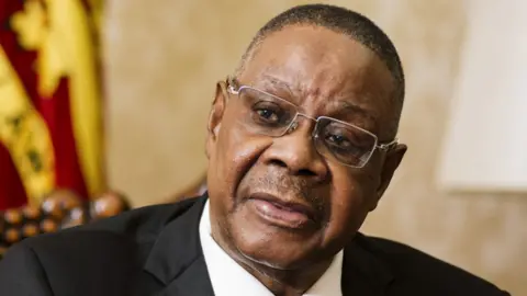 Bloomberg via Getty Images A close-up shot of Peter Mutharika wearing silver-rimmed glasses and a suit