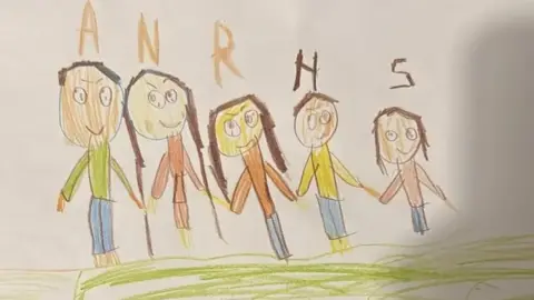 A colourful child's drawing, by seven year-old Sara of her family holding hands in a row, smiling. The first initial of each family member's name has been written above their heads.