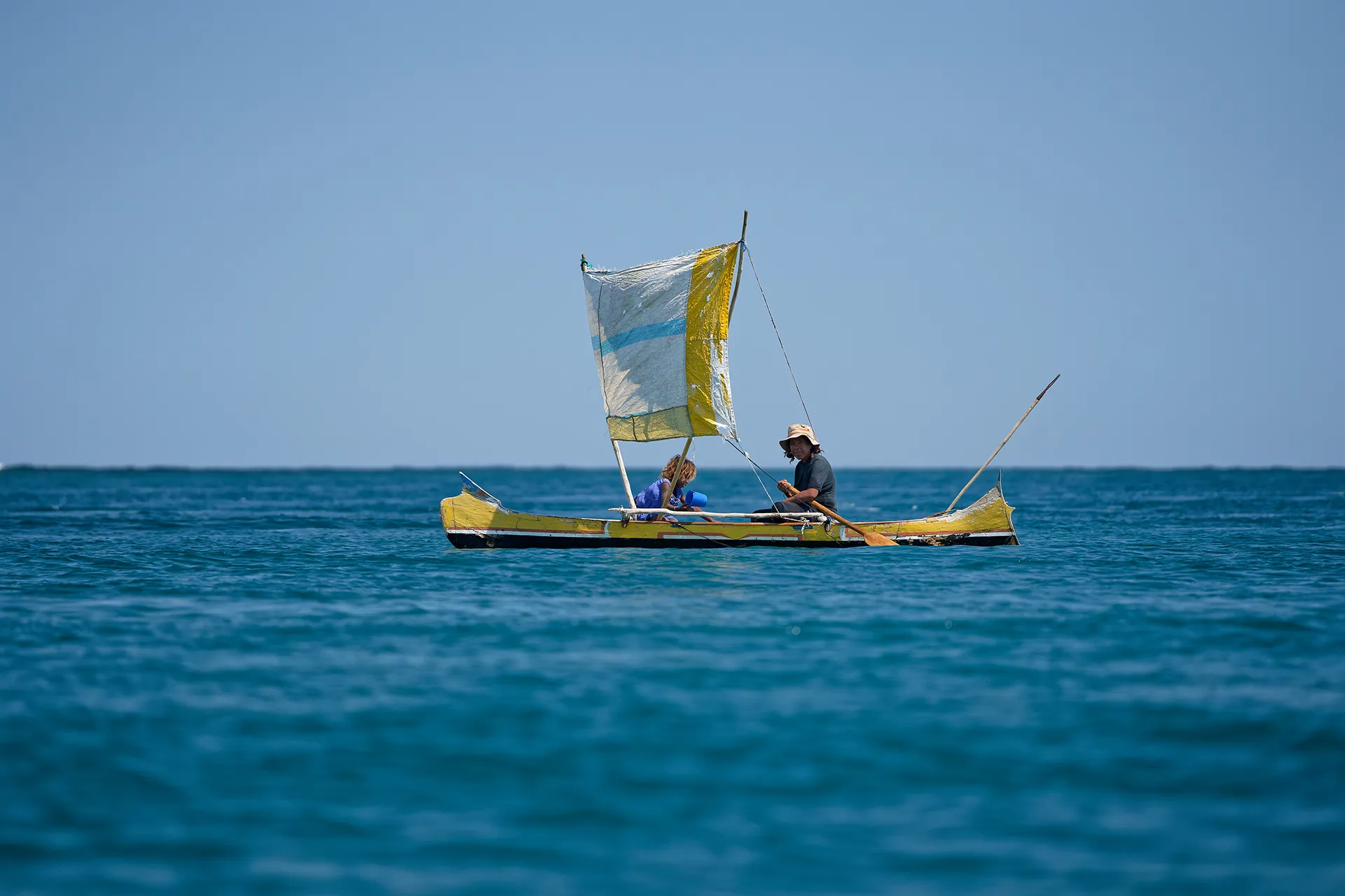A woman and her granddaughter sailing in a yellow pirogue.