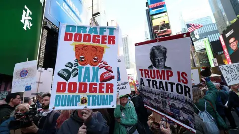 Getty Images Protestors hold signs in Times Square that read "draft dodger, tax dodger: dump Trump" and "Trump is a traitor".