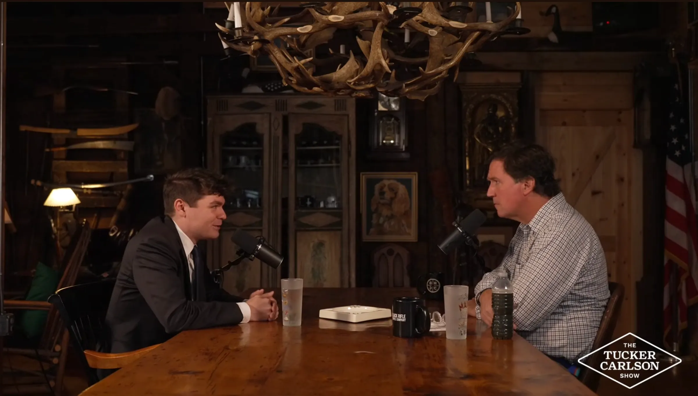 Two white men sitting across a wooden table with microphones in front of them