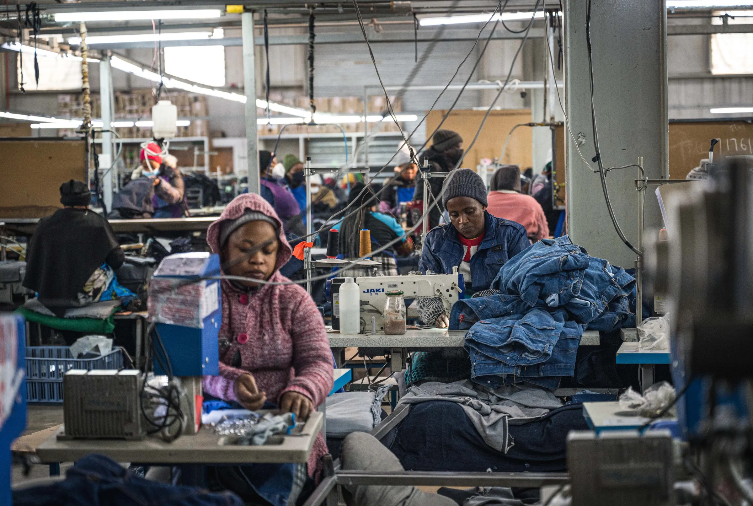 Garment workers in Lesotho sit at tables and sewing machines, working on piles of clothing.