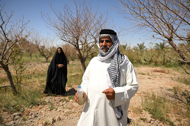 A man holds a bottle of cloudy water in the farm of Iraqi farmer Zuleikha Hashim Taleb